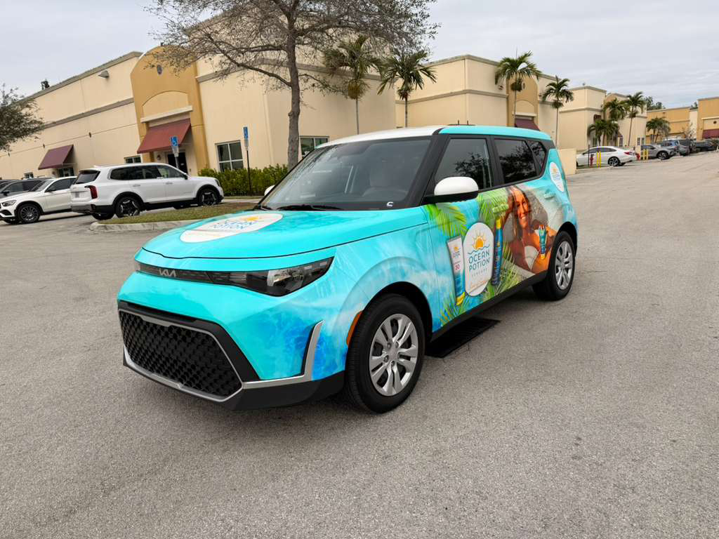 Turquoise promotional SUV with Ocean Potion branding and tropical graphics parked in a parking lot outside a strip mall.