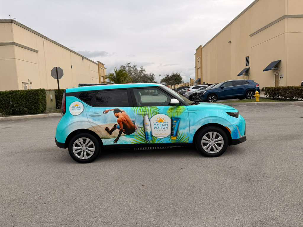 Turquoise promotional SUV wrapped with Ocean Potion branding, featuring a surfer graphic and product bottles on the side park lot.