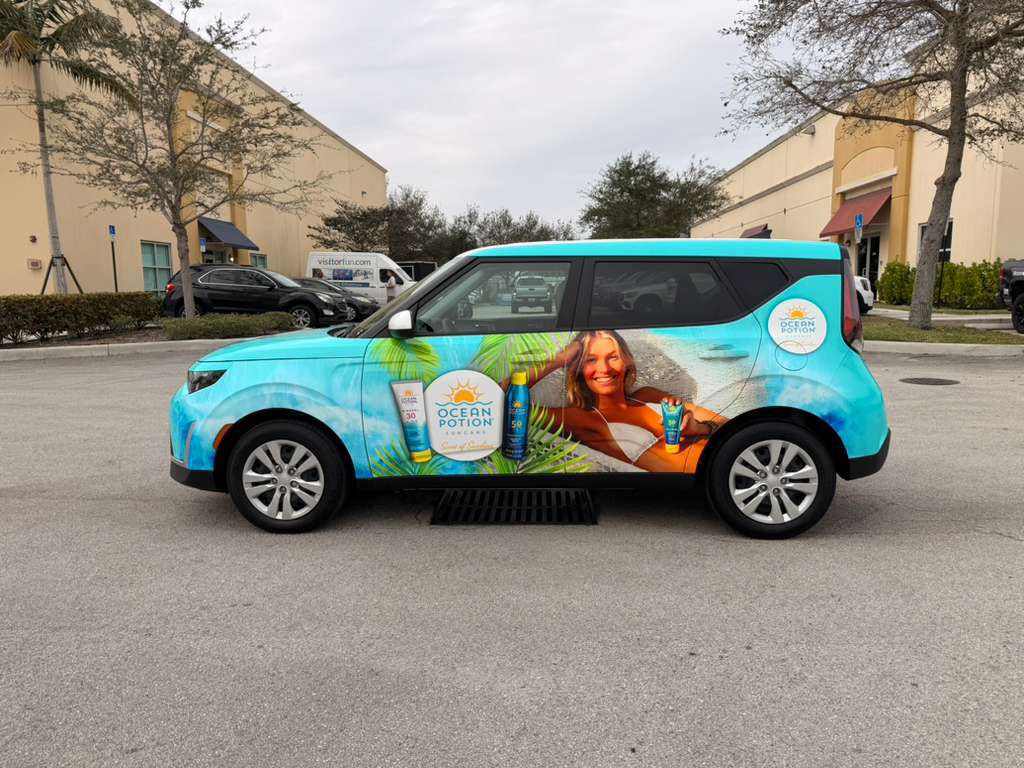 Turquoise promotional SUV wrapped with Ocean Potion sunscreen ads, featuring a smiling woman lounging and product bottles on the side window.