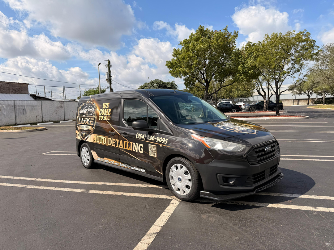 Black detailing van parked in a lot with gold Luxe Auto Detailing decals on the side and 'We Come to You' wording nearby.