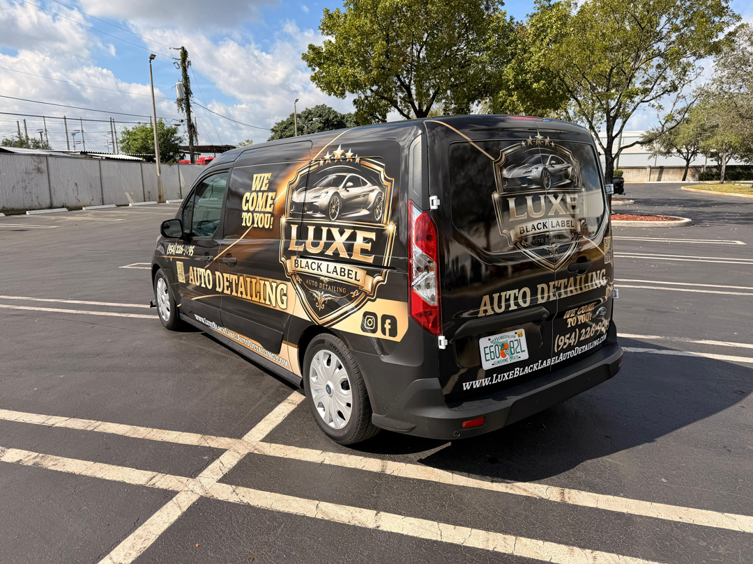 Black van wrapped with Luxe Black Label Auto Detailing branding, parked in a lot with gold crest graphics
