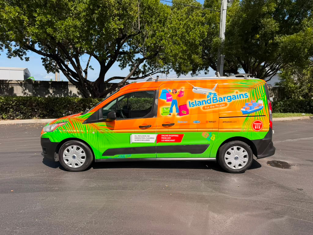 Bright orange and lime-green Island Bargains delivery van parked on a street with trees, featuring promotional graphics and the brand name Island Bargains on the side.