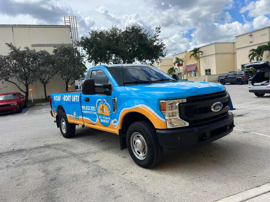 Blue Ford service pickup wrapped with boat-lifts branding and wave graphics, parked in a lot.