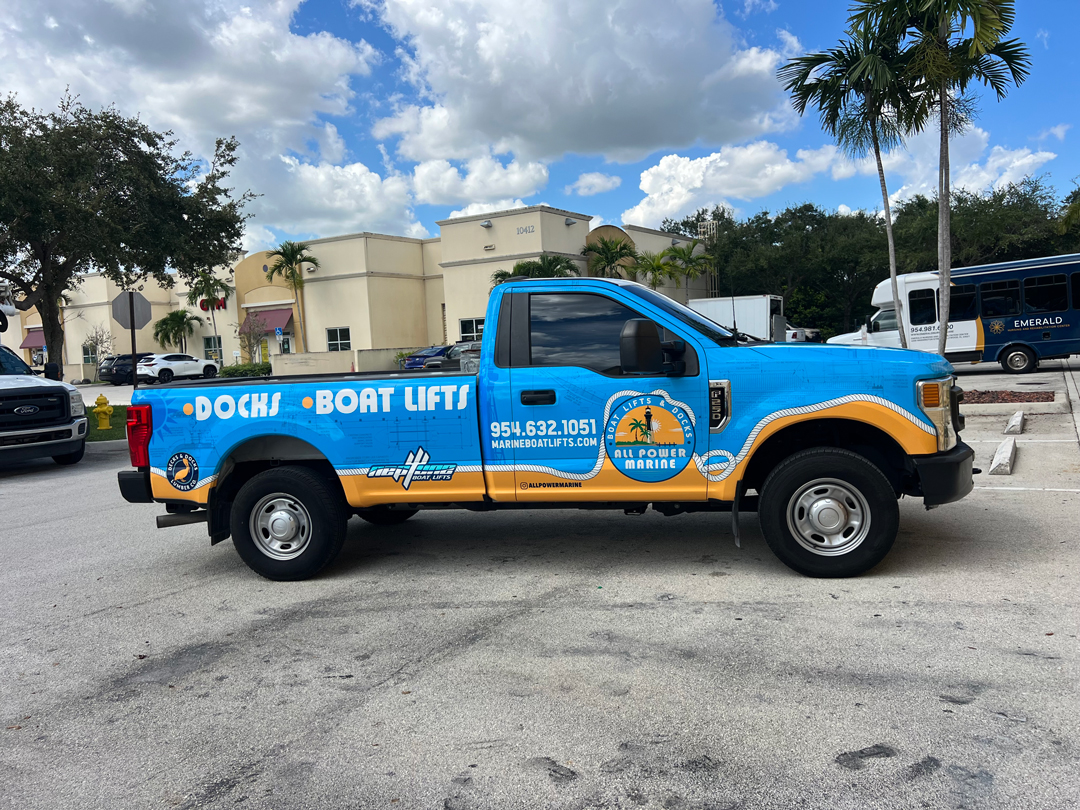 Blue and orange pickup truck advertising boat docks and lifts, with palm-tree logo and contact number on the door.