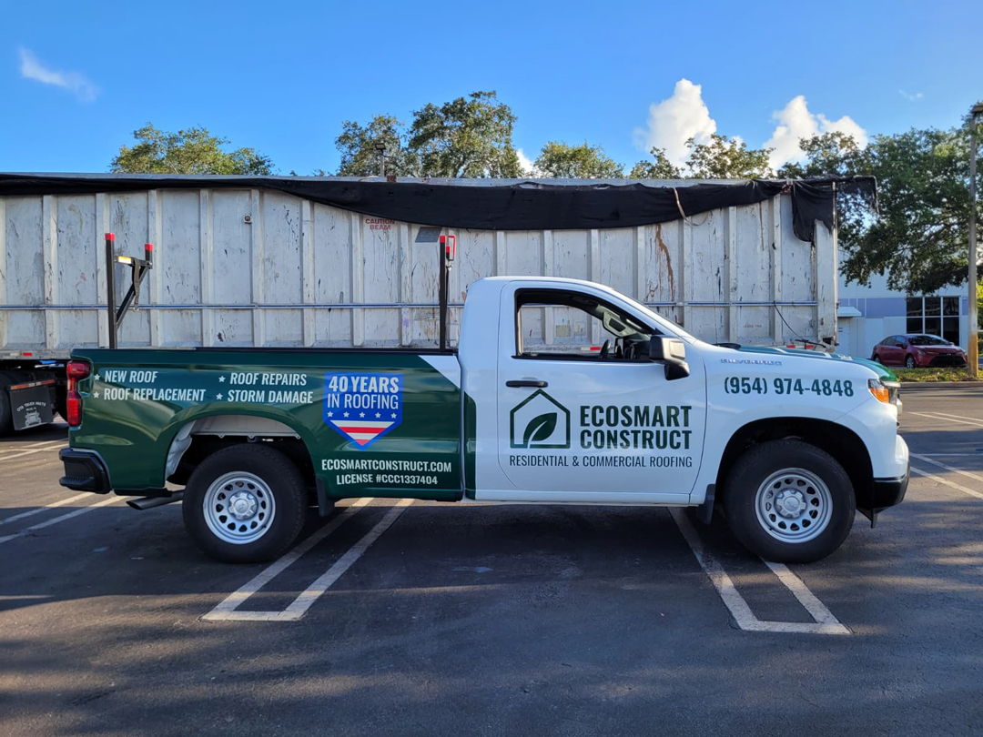 White and green ECOSMART CONSTRUCT pickup truck parked in a lot, advertising residential & commercial roofing with phone number on the door and a '40 years in roofing' graphic.