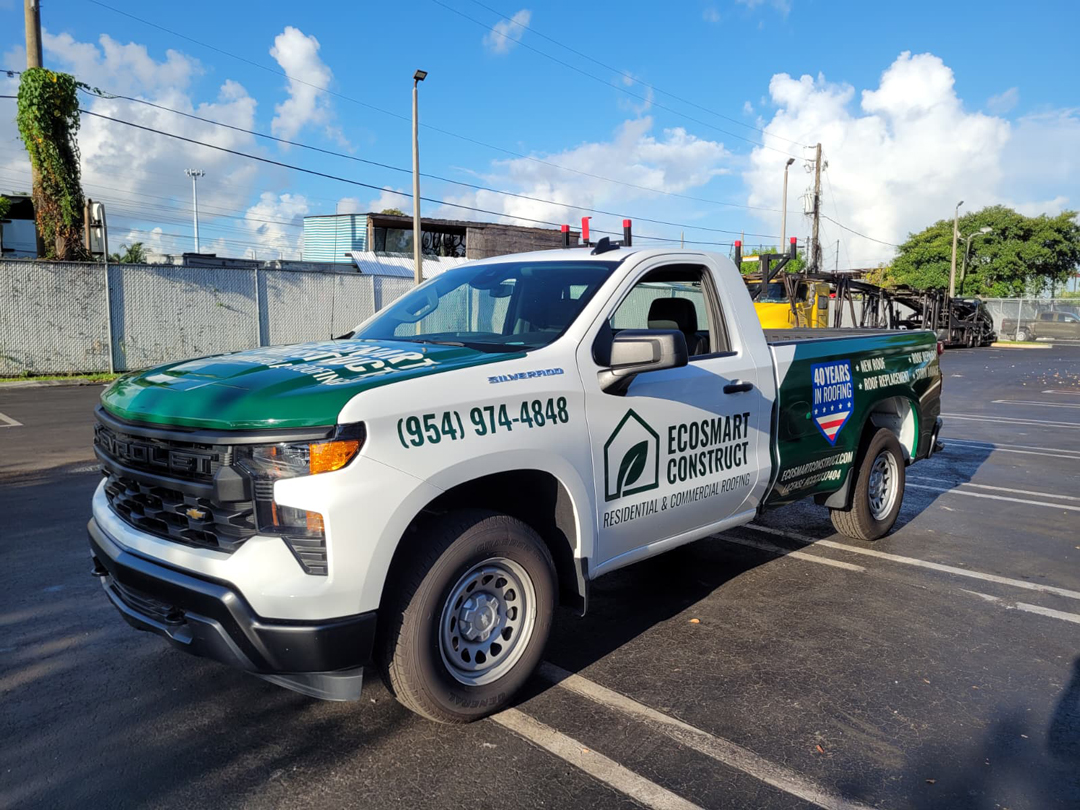 White EcoSmart Construct pickup parked in a lot, green hood and logo, phone number (954) 974-4848, roofing services advertised on the side.