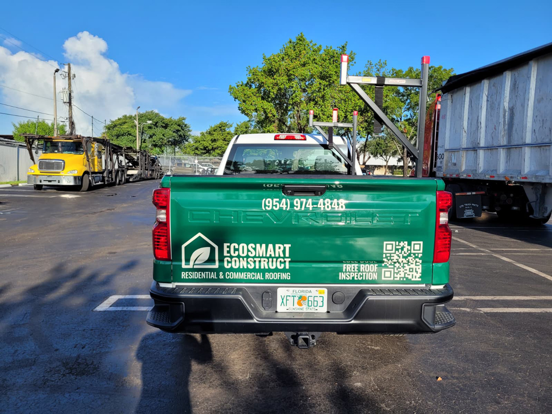 Back of a green Ecosmart Construct pickup truck in a parking lot, with roofing company graphics and phone number on the tailgate.