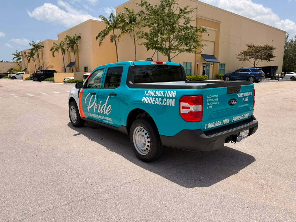 Teal Pride service pickup truck parked in a lot near beige commercial buildings, with the Pride logo and contact info on the side.