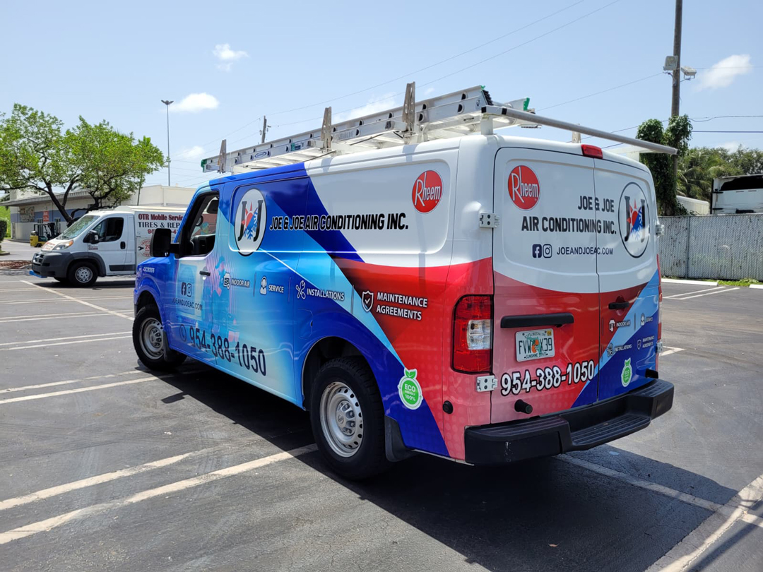 Company service van for Joe & Joe Air Conditioning Inc. with ladder rack, colorful blue-red wrap, contact number 954-388-1050, on a parking lot.