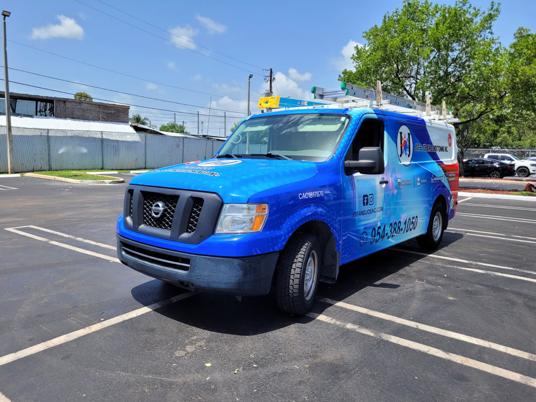 Blue service van with a ladder rack on top parked in a lot, with company branding on the side and a green tree backdrop.