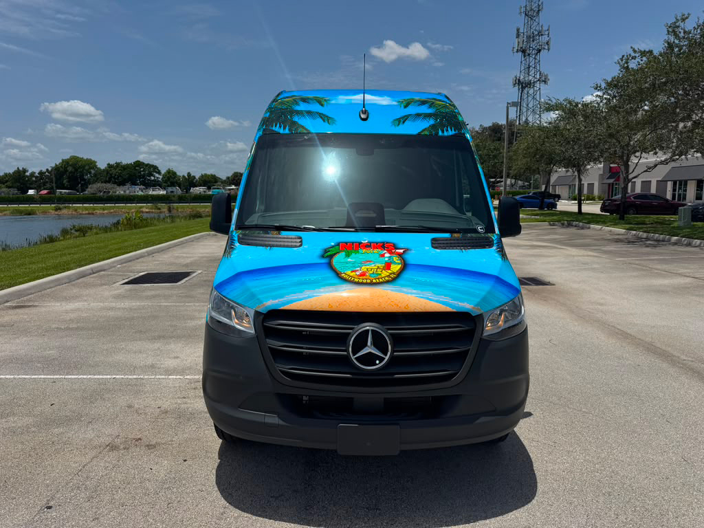 Front view of a blue Mercedes van with a tropical beach wrap and Nick's logo on the hood.