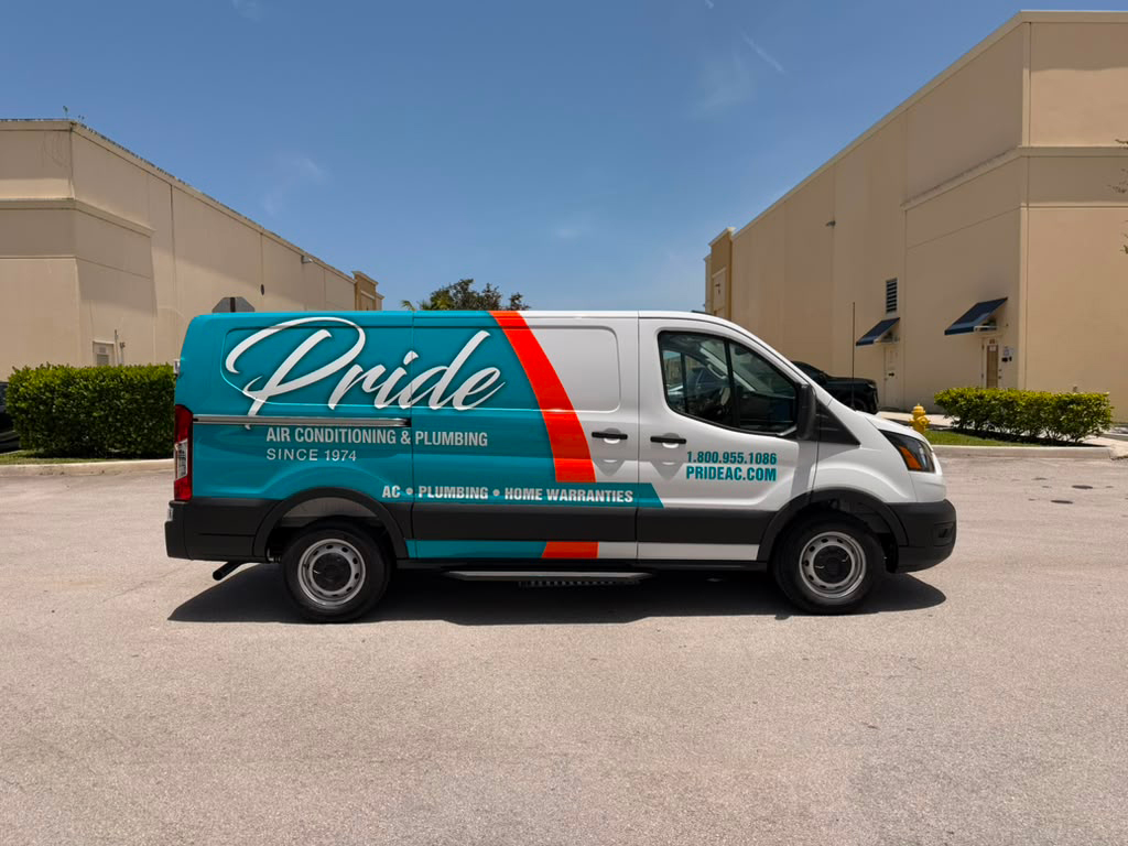 teal Pride Air Conditioning & Plumbing van with large script 'Pride' logo parked in a lot, building warehouses in the background