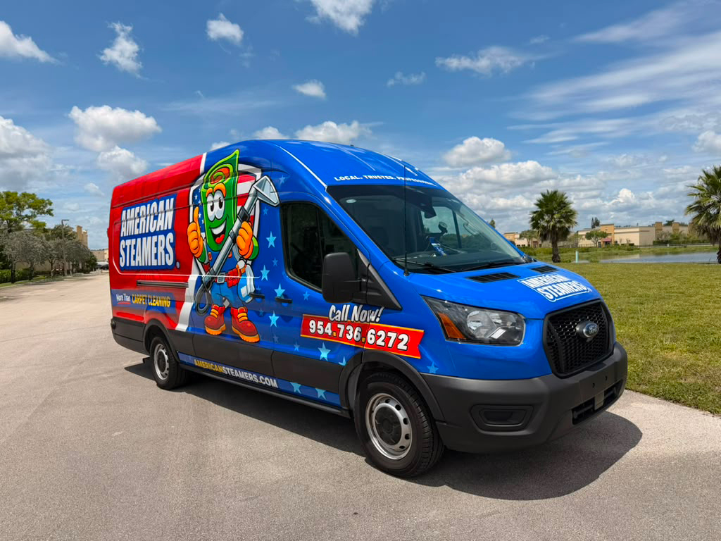 Blue American Steamers delivery van featuring a cartoon mascot, parked on a sunny street near a grassy area.