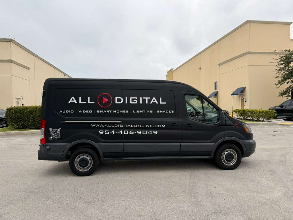 Black All Digital promotional van parked in a lot, displaying logo and services (audio, video, smart homes, lighting, shades); website alldigitalonline.com and phone 954-406-9049 are visible.