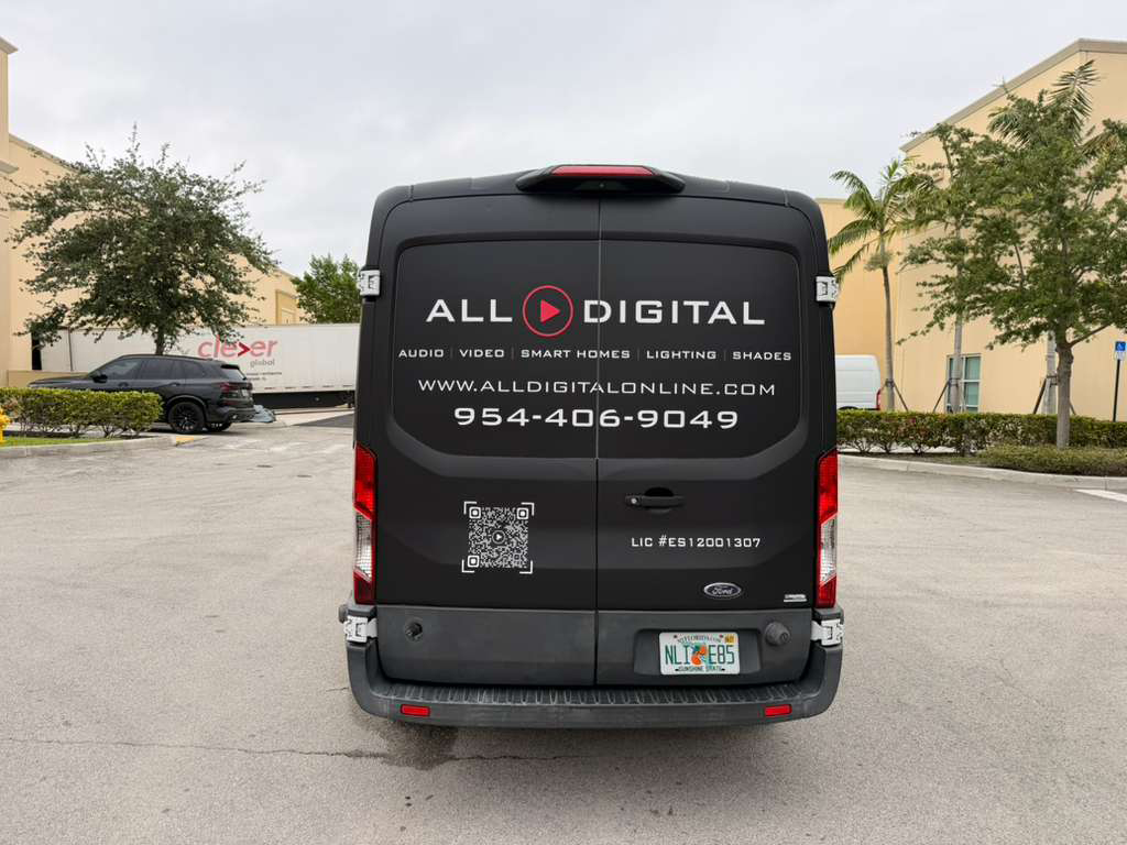 Rear view of a black ALL DIGITAL van with logo, phone number, and QR code in a parking lot.