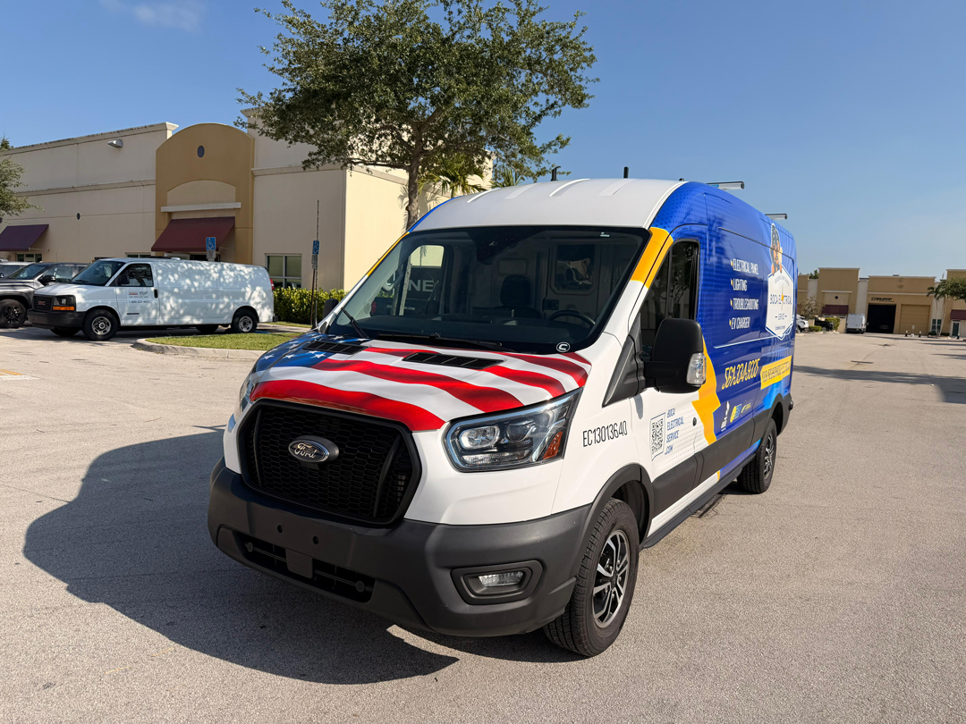 Patriotic white and blue Ford cargo van with a red‑white‑blue hood design parked in a lot by a beige shopping center.