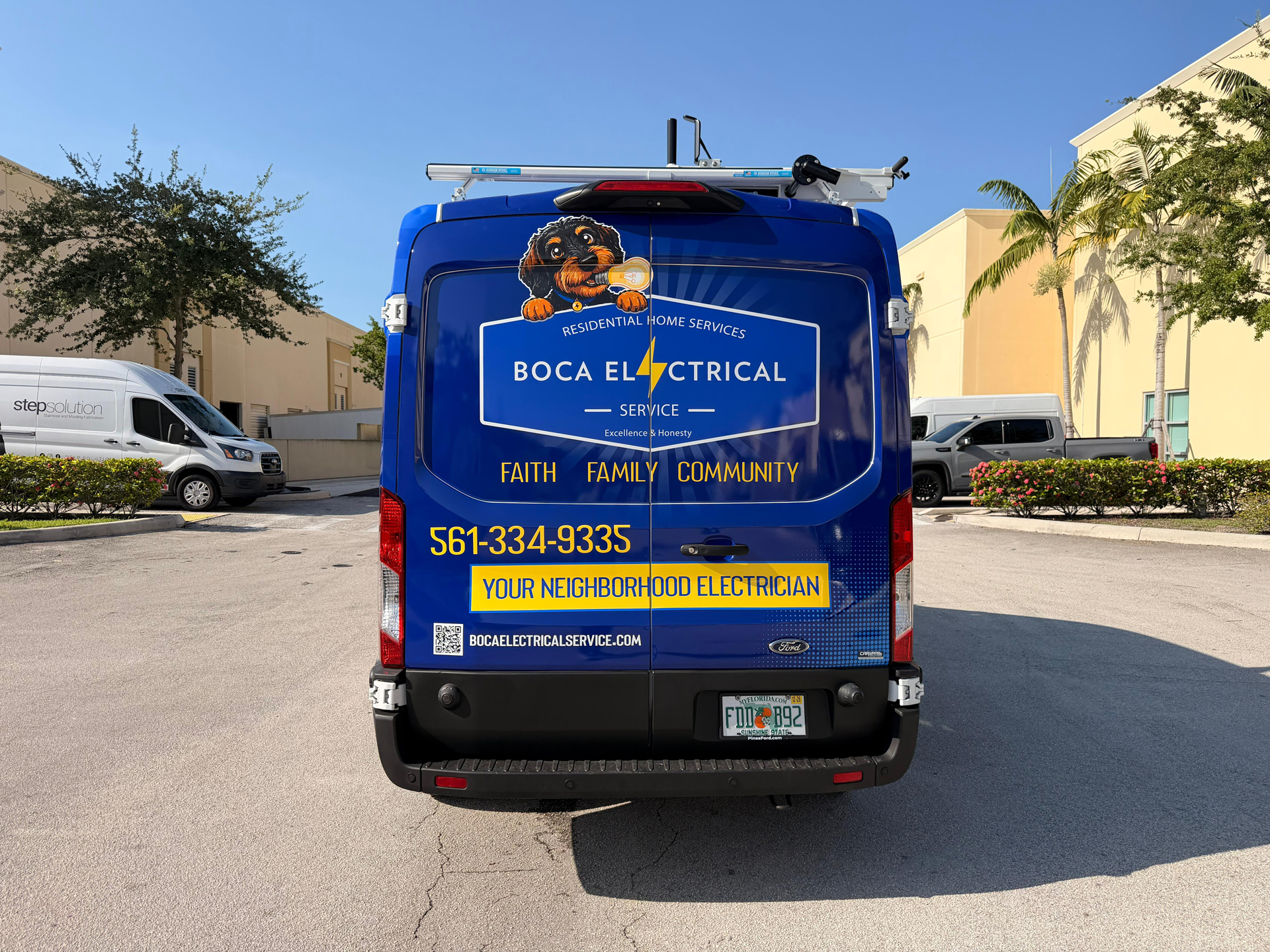 Blue Boca Electrical Service van parked in a lot, displaying the dog mascot, ladder on top, and 'Your Neighborhood Electrician' messaging on the back doors.