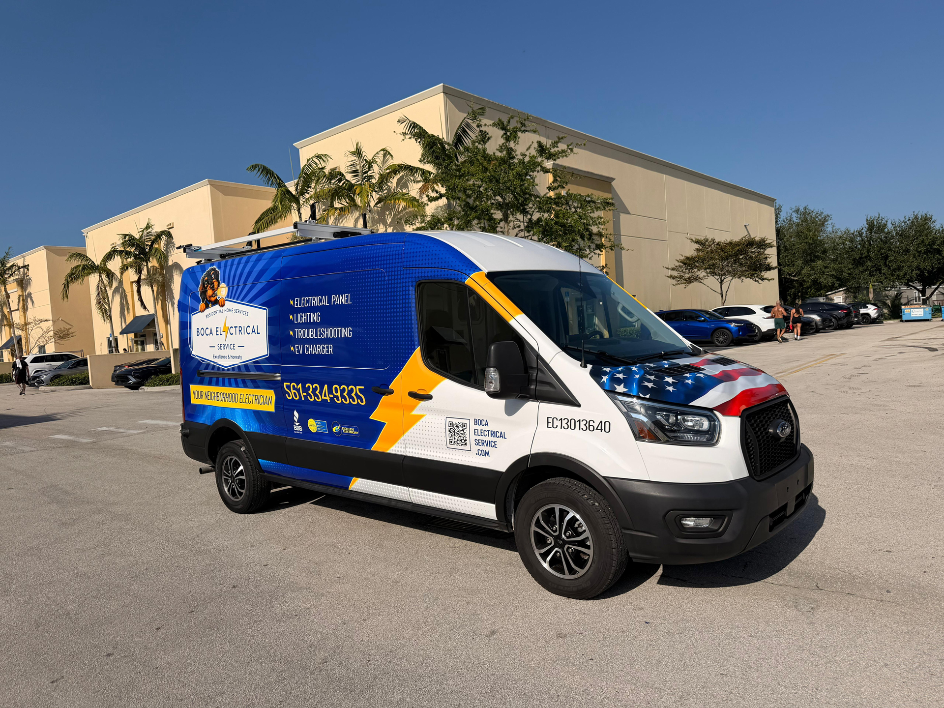 Blue Boca Electrical Service van with ladder rack parked in a lot beside a beige commercial building, palm trees in the background.
