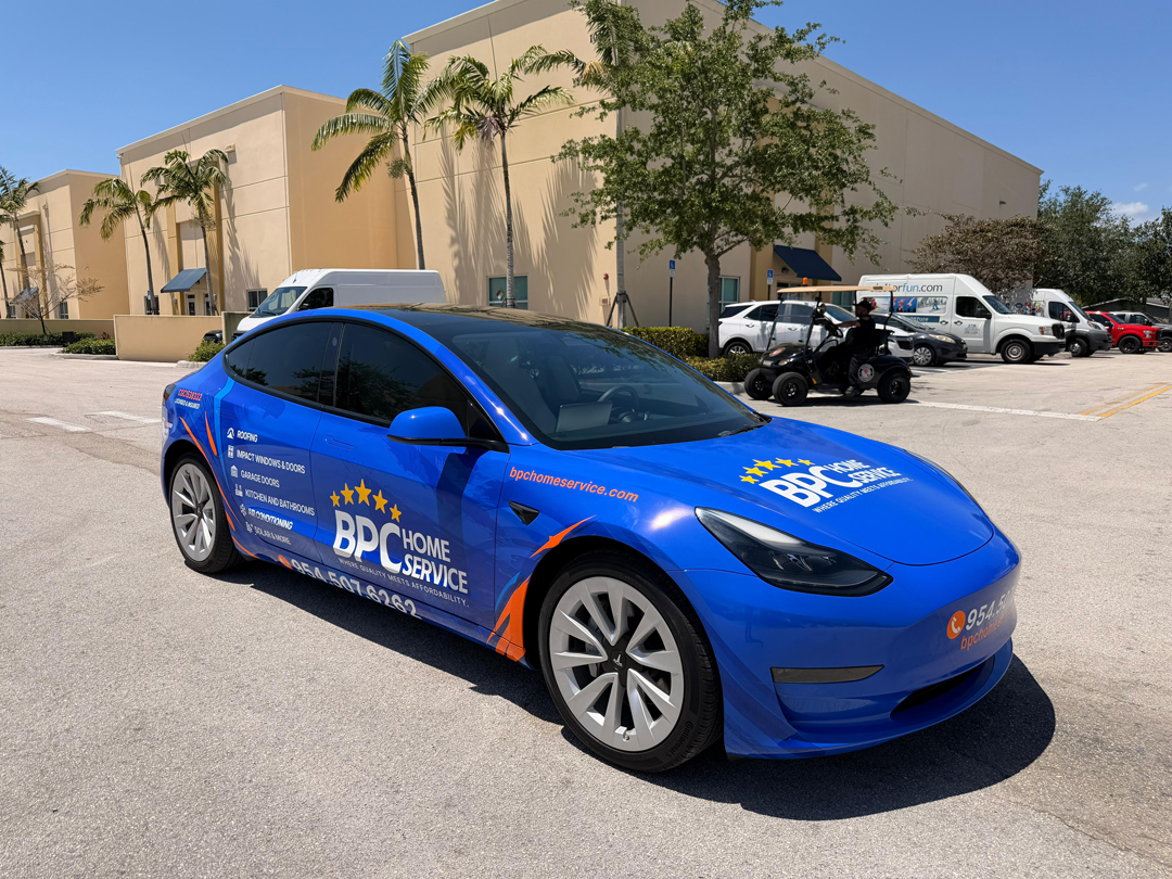 Blue Tesla with BPC Home Service advertising wrap parked in a lot near a beige commercial building.